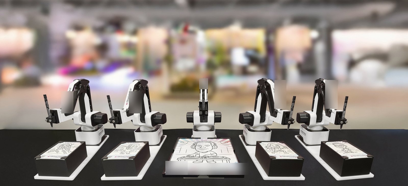 Five robot arms at an event, each drawing a portrait on paper